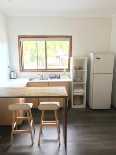 a kitchen with a table and two stools and a refrigerator at Arts Factory by Nomads in Byron Bay
