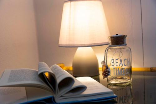 an open book on a table with a lamp and a bottle at Villa Curiazzi Guesthouse Viale la Pelosa 16 in Stintino