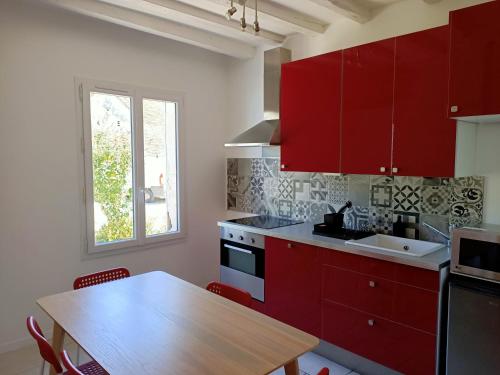 a kitchen with red cabinets and a wooden table at La Little House - Proche ZOOPARC de Beauval in Saint-Jean-Saint-Germain