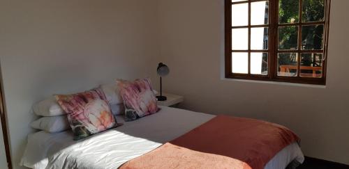 a bedroom with a bed with pillows and a window at Home2Home Protea Cottage in Port Elizabeth