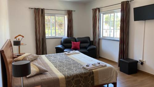 a bedroom with a bed and a chair and windows at Lagoa Albufeira House in Sesimbra