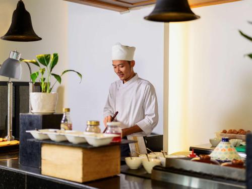 a chef standing in a kitchen preparing food at The Lake Garden Nay Pyi Taw - MGallery Collection in Nay Pyi Taw