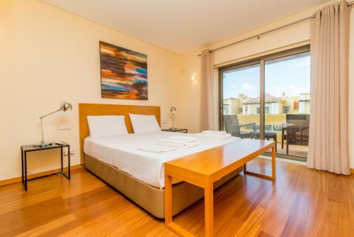 1 dormitorio con cama, escritorio y ventana grande en Alecrim Lux Tavira Residence Villa 4M, en Luz de Tavira