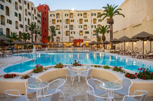 une piscine d'hôtel avec des chaises, des tables et des bâtiments dans l'établissement Hotel Hopps, à Mazara del Vallo