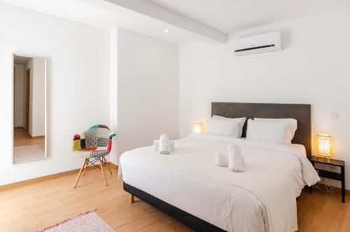 a white bedroom with a large bed and a chair at North Breeze - 2 Bedroom Apartment with Rooftop Pool in Nazaré