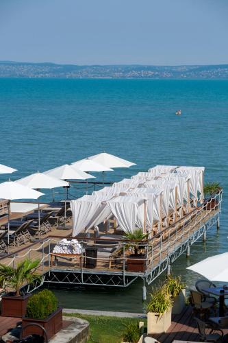 a pier with tables and umbrellas on the water at Mala Garden Design Hotel in Siófok