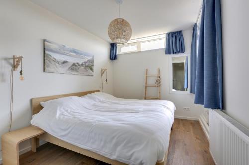 a bedroom with a large white bed with blue curtains at DE TRINTEL met zeezicht in Egmond aan Zee
