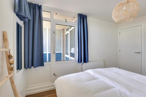 a bedroom with a bed and blue curtains and a mirror at DE TRINTEL met zeezicht in Egmond aan Zee