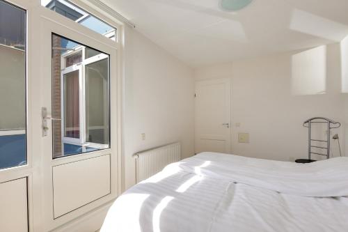 a white bedroom with a bed and a window at DE TRINTEL met zeezicht in Egmond aan Zee