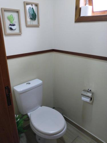 a white toilet in a bathroom with two pictures on the wall at Chalés do Pardal in Visconde De Maua
