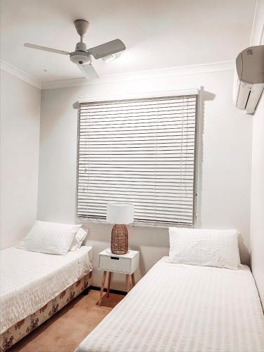 a bedroom with two beds and a window with a fan at Carnarvon 3BR & 2BA Holiday House in Carnarvon
