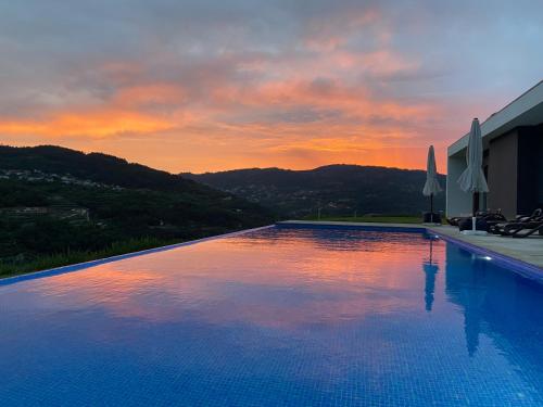 a large swimming pool with a sunset in the background at Casa de Ribadouro in Baião