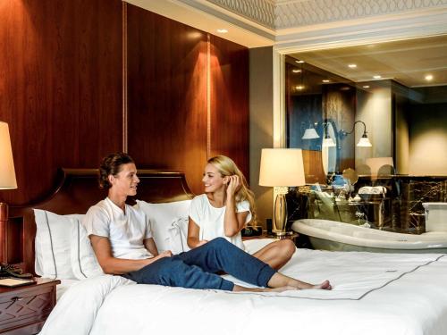a man and a woman sitting on a bed in a hotel room at Hotel Muse Bangkok Langsuan - MGallery - SHA EXTRA PLUS in Bangkok
