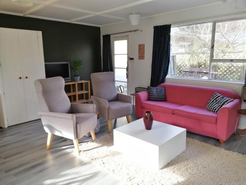 a living room with a red couch and two chairs at Cozy guesthouse at the Rabbithole, Akatarawa Valley in Upper Hutt