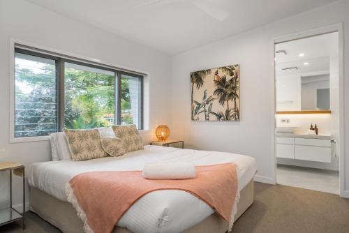 a white bedroom with a large bed with an orange blanket at Foam in Byron Bay