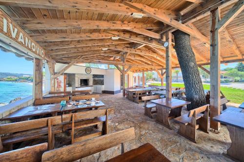 a restaurant with wooden tables and benches and the ocean at Apartments & Bungalows Ivanović in Kaštela