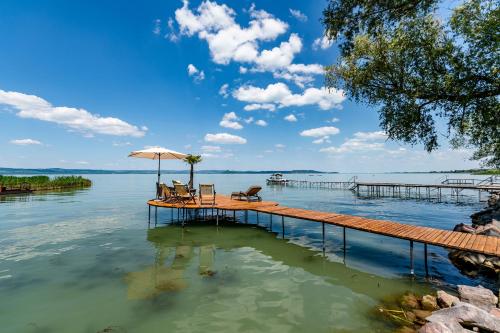 a dock with chairs and an umbrella on the water at Viktoria House in Balatonszárszó