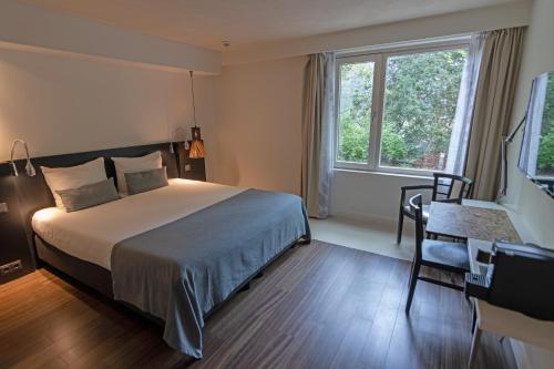 a bedroom with a bed and a desk and a window at Hotel Landgoed Zonheuvel in Doorn