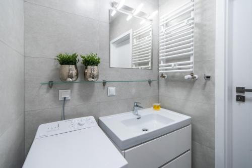 La salle de bains blanche est pourvue d'un lavabo et d'un miroir. dans l'établissement Blue Sea Apartamenty Kasprowicza, à Kołobrzeg