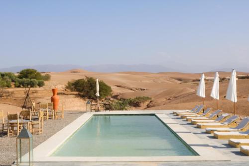 a swimming pool in the desert with chairs and umbrellas at Emeraude Camp Agafay in El Karia