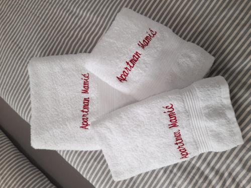 two white towels with writing on them on a bed at Apartmani Mamić in Tomislavgrad