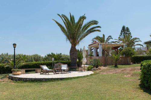 a patio with two chairs and a palm tree at Palmaya Villa, unique seafront experience in Vaia