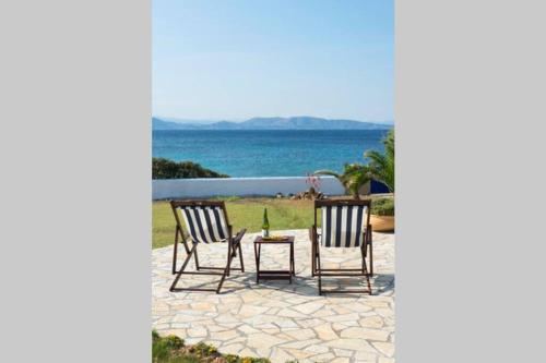 a patio with two chairs and a table and the ocean at Palmaya Villa, unique seafront experience in Vaia