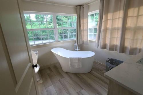 La salle de bains est pourvue d'une baignoire blanche et d'une fenêtre. dans l'établissement Farm House stay with soaking tub and hot tub barn, à Hammond