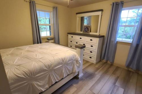 a bedroom with a bed and a dresser and windows at Farm House stay with soaking tub and hot tub barn in Hammond