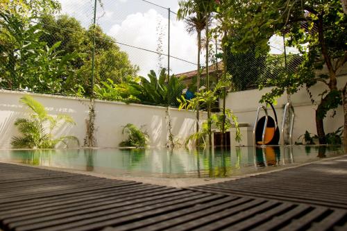 a swimming pool next to a white wall with trees at Ellen's Place in Colombo