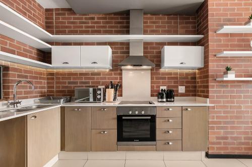a kitchen with brown cabinets and a brick wall at Easy Stay - The Vantage Rosebank in Johannesburg