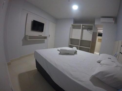 a bedroom with a bed with white sheets and a tv at Apart Hotel CTC - Edifício Araras in Caldas Novas