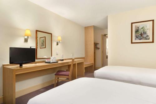 a hotel room with two beds and a desk with a television at Days Inn by Wyndham Sevenoaks Clacket Lane in Westerham