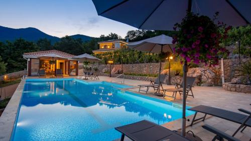 a swimming pool with an umbrella and a house at Apartments Villa BV in Opatija