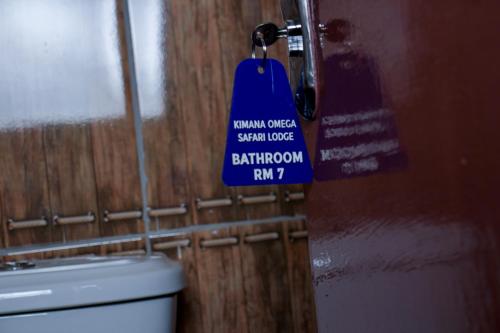 a blue sign hanging on a door in a bathroom at Kimana Omega Safari Lodge in Kimana
