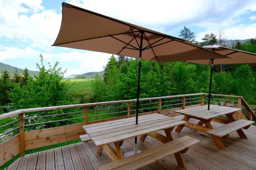 two picnic tables with an umbrella on a deck at Gite des Rosiers in Lans-en-Vercors