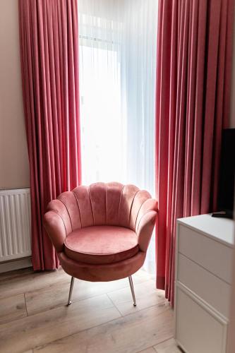 a brown chair sitting in front of a window with red curtains at Apartament Bella Rosa z podziemnym parkingiem in Kielce