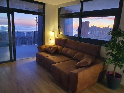 a brown couch in a living room with large windows at Sunset Waves Benidorm by KalmaRent in Benidorm