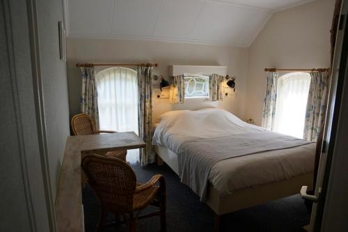 a bedroom with a bed and a table and two windows at Pension De Hoestinkhof in Markelo