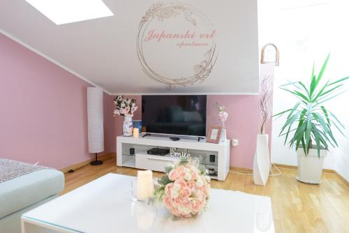 a living room with a tv and flowers on a table at Apartman Japanski vrt, Centar in Vrnjačka Banja