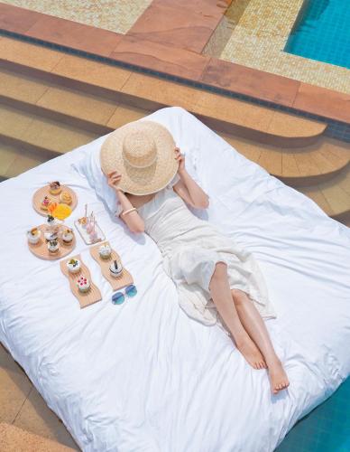 a woman wearing a straw hat laying on a bed at Pullman Sanya Yalong Bay Villas & Resort in Sanya
