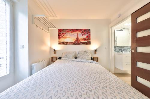 a bedroom with a white bed with a painting on the wall at Studio Le Rosier - Paris Gare du Nord en 15 min - in Deuil-la-Barre