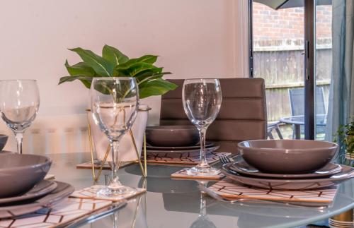 a table with glasses and plates and a plant on it at CENTRAL MK- 3Bed, 2 Bath house for LONG TERM CONTRACTOR Stays, free parking for 2 vehicles, DESK & GARDEN space managed by CHIQUE PROPERTIES LTD in Milton Keynes