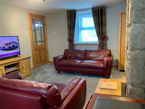 sala de estar con sofás de cuero y TV de pantalla plana en No 10 The Cottage, en Inverness
