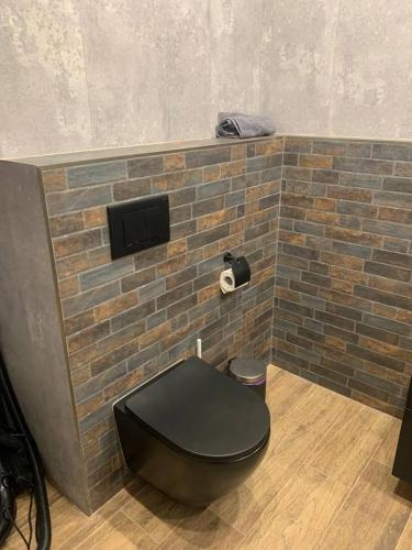 a toilet with a black seat and a brick wall at Apartament Batory in Toruń