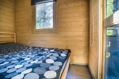 a bed in a room with wooden walls and windows at Metsaääre Accommodation in Uulu