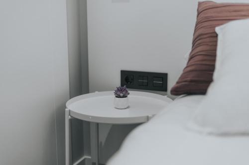a small white table with a plant on it next to a bed at Apartamentos MK77 León - Palomera in León