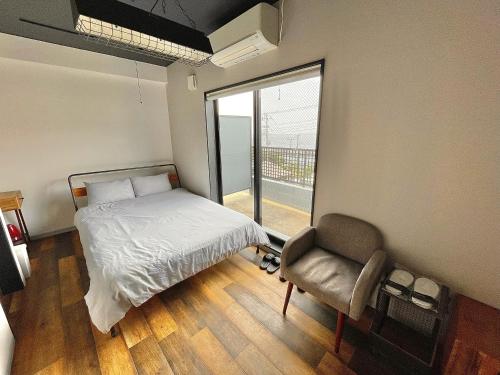a bedroom with a bed and a chair and a window at Book Tea Bed IZUOSHIMA in Oshima
