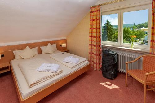 a bedroom with a bed and a chair and a window at KIShotel am Kurpark in Bad Soden-Salmünster