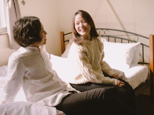 a woman sitting on a bed talking to another woman at Guesthouse Hitoyado in Shizuoka